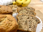 Slices of banana bread with bananas, walnuts, yellow bananas, whole loaf in the background